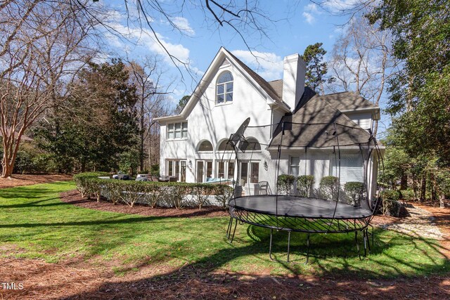 back of property featuring a lawn, a chimney, and a trampoline