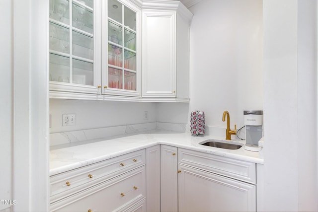 kitchen with light stone counters, white cabinetry, glass insert cabinets, and a sink
