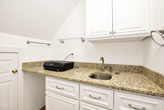 kitchen featuring white cabinetry, light stone counters, and a sink