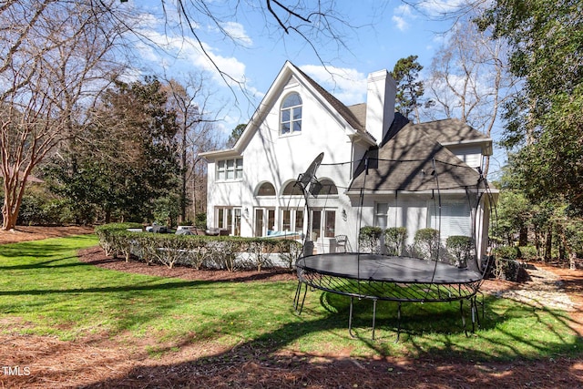rear view of property with a yard, a trampoline, a chimney, and stucco siding