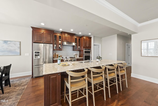 10529 Sablewood Dr Unit 111, Raleigh, NC 27617 - kitchen with stainless steel appliances, under cabinet range hood, a kitchen island with sink, baseboards, and dark wood-style flooring