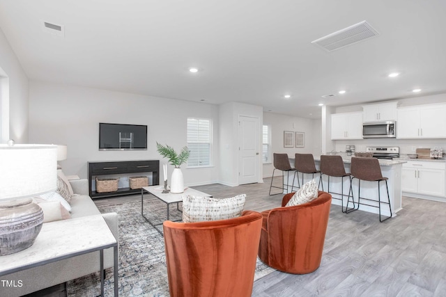 living area featuring recessed lighting, light wood finished floors, and visible vents