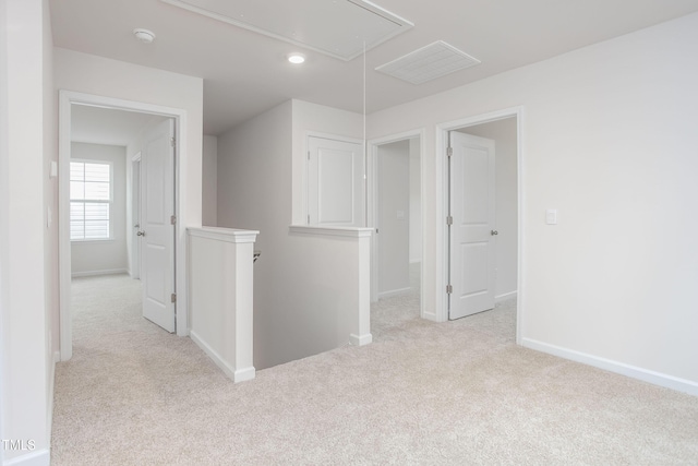 carpeted empty room with visible vents, baseboards, and attic access