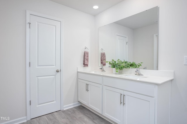 bathroom featuring a sink, baseboards, double vanity, and wood finished floors