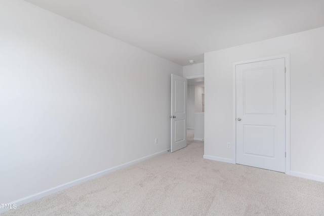 spare room with baseboards and light carpet