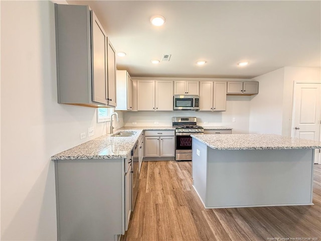2224 Roadster Pony Rd, Hope Mills, NC 28348 - kitchen featuring appliances with stainless steel finishes, gray cabinets, light wood-type flooring, a kitchen island, and light stone countertops