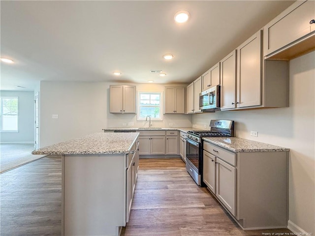 2224 Roadster Pony Rd, Hope Mills, NC 28348 - kitchen with stainless steel appliances, a kitchen island, gray cabinets, light wood finished floors, and light stone counters