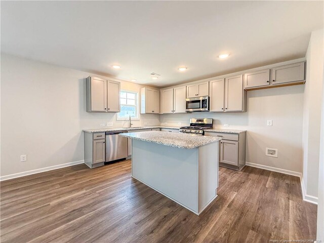 2224 Roadster Pony Rd, Hope Mills, NC 28348 - kitchen with appliances with stainless steel finishes, gray cabinetry, dark wood-style flooring, a kitchen island, and light stone countertops