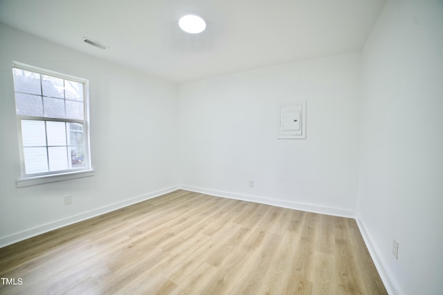 empty room featuring light wood finished floors, visible vents, electric panel, and baseboards