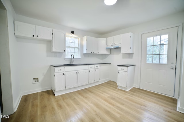 kitchen with a sink, light wood-type flooring, dark countertops, and under cabinet range hood