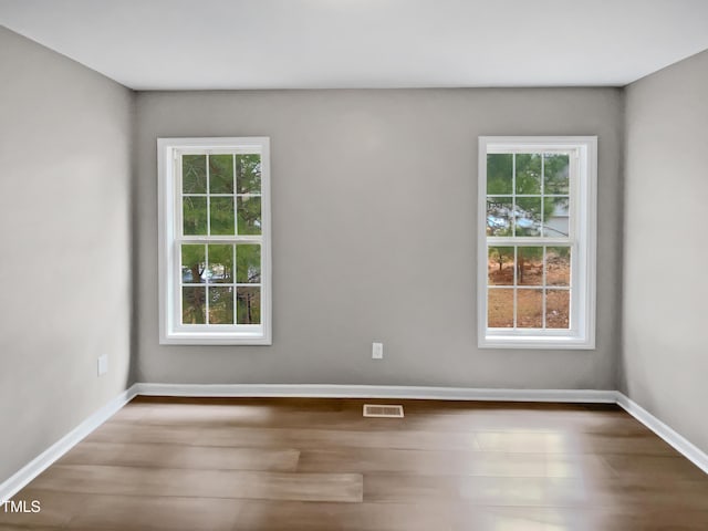 empty room featuring wood finished floors, visible vents, a wealth of natural light, and baseboards