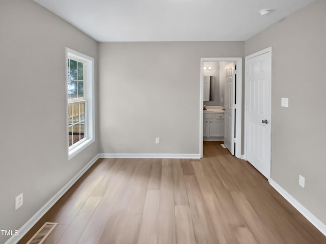 unfurnished bedroom featuring visible vents, light wood-style floors, baseboards, and ensuite bathroom