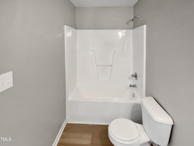 bathroom with washtub / shower combination, toilet, wood finished floors, and baseboards