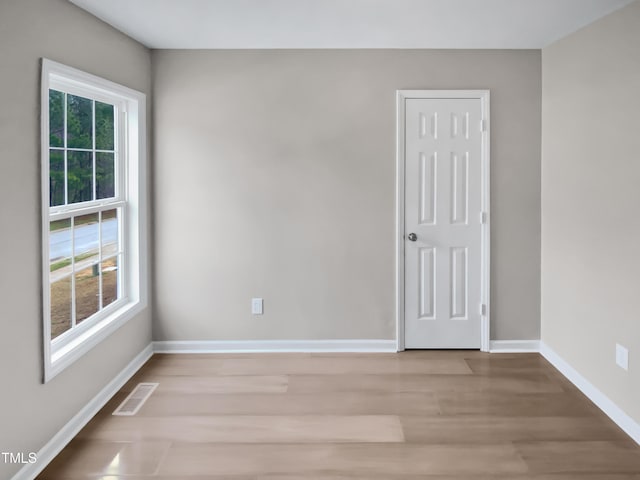 spare room with visible vents, plenty of natural light, baseboards, and wood finished floors