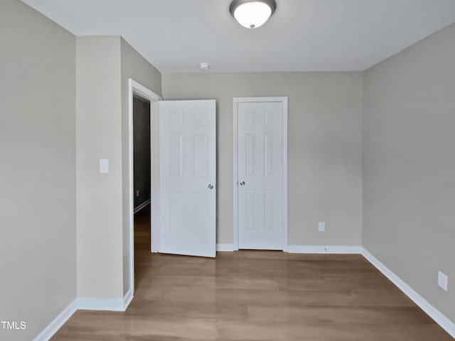 unfurnished bedroom featuring wood finished floors, baseboards, and a closet