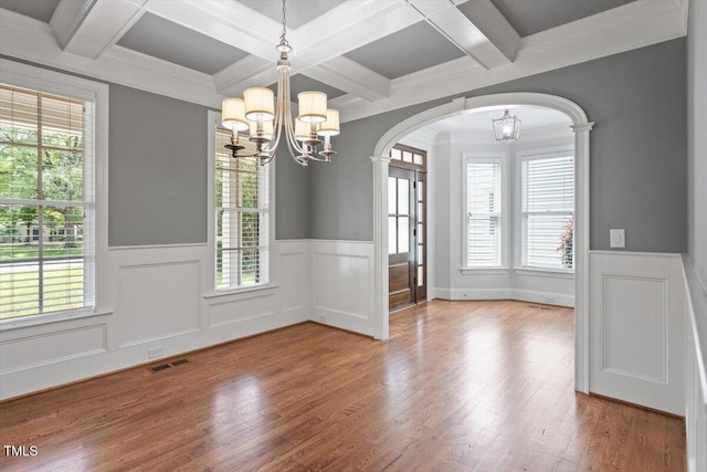 unfurnished dining area featuring an inviting chandelier, arched walkways, a wainscoted wall, wood finished floors, and visible vents