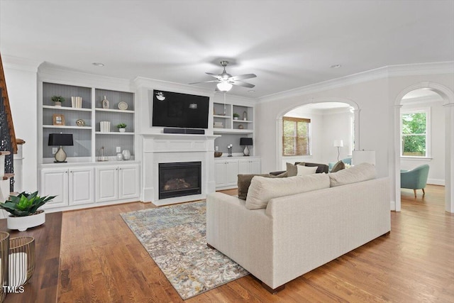 living room with crown molding, arched walkways, ceiling fan, and a wealth of natural light