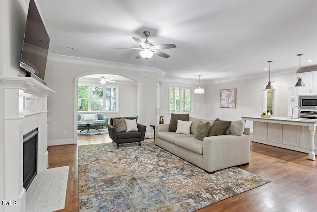 living area with arched walkways, ceiling fan, wood finished floors, and a fireplace