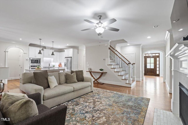 living room with arched walkways, stairs, a ceiling fan, and ornamental molding