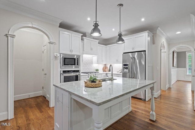 kitchen with ornamental molding, a sink, white cabinetry, arched walkways, and stainless steel appliances
