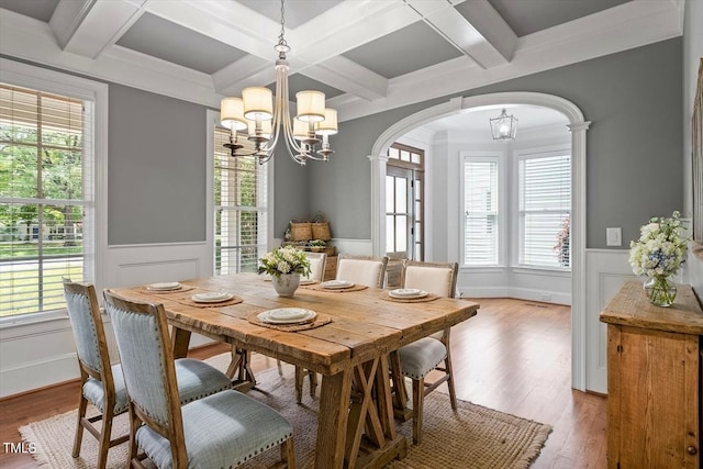 dining area with arched walkways, an inviting chandelier, light wood finished floors, and coffered ceiling