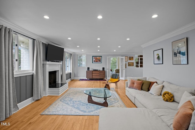 living area featuring recessed lighting, a fireplace with raised hearth, ornamental molding, and light wood-style flooring