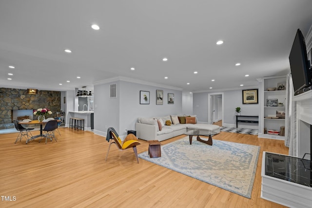 living room featuring ornamental molding, a fireplace, recessed lighting, and wood finished floors