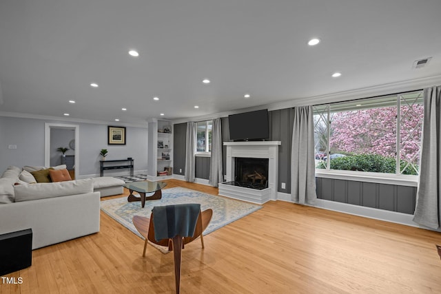 living area featuring crown molding, light wood finished floors, a fireplace with raised hearth, recessed lighting, and visible vents
