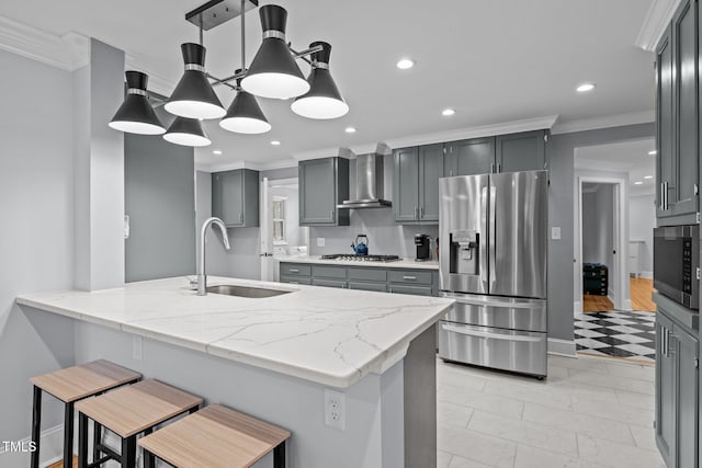kitchen with ornamental molding, light stone countertops, wall chimney range hood, a sink, and stainless steel appliances
