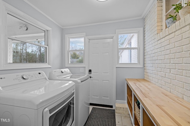 washroom featuring laundry area, washing machine and dryer, brick wall, and a healthy amount of sunlight