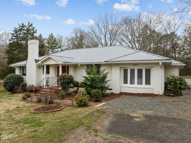 ranch-style house featuring a chimney, a front lawn, metal roof, and brick siding