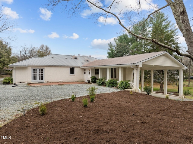 rear view of house with brick siding, driveway, french doors, and metal roof