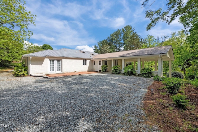 view of front facade with brick siding, french doors, driveway, and metal roof