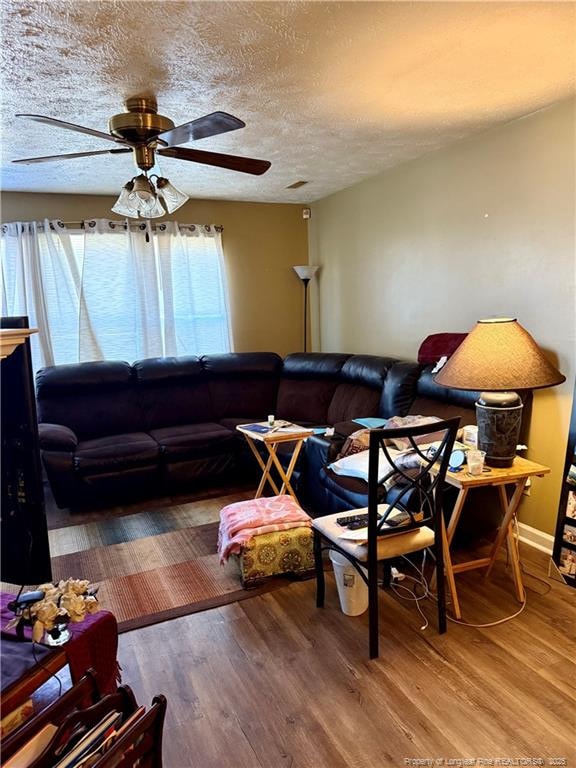 living room featuring baseboards, a textured ceiling, wood finished floors, and a ceiling fan