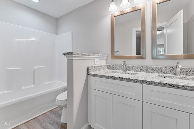 bathroom with toilet, a sink, double vanity, and wood finished floors