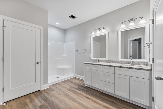 full bathroom with double vanity, a sink, a walk in shower, and wood finished floors