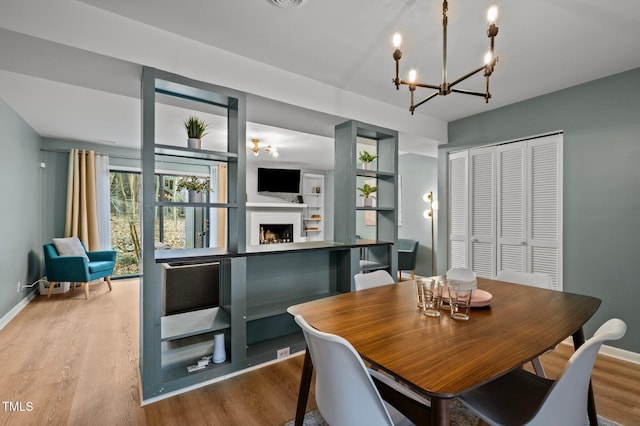 dining area featuring a fireplace, baseboards, an inviting chandelier, and wood finished floors