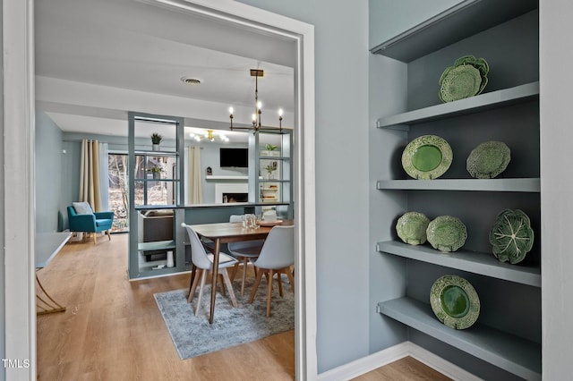 dining space with visible vents, built in shelves, wood finished floors, baseboards, and a chandelier