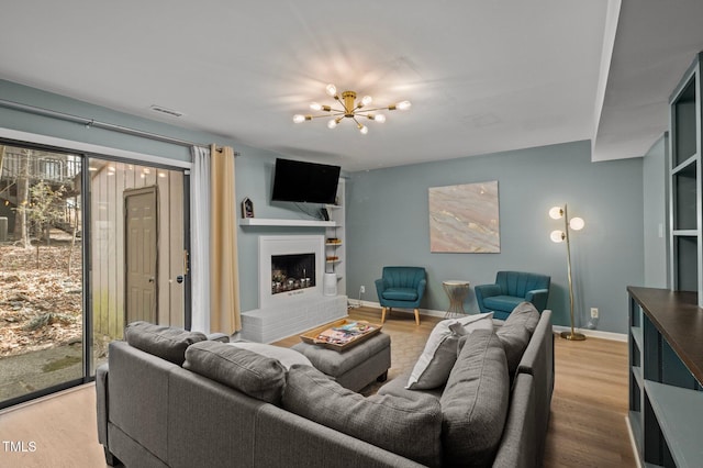 living area with a brick fireplace, wood finished floors, baseboards, and a chandelier