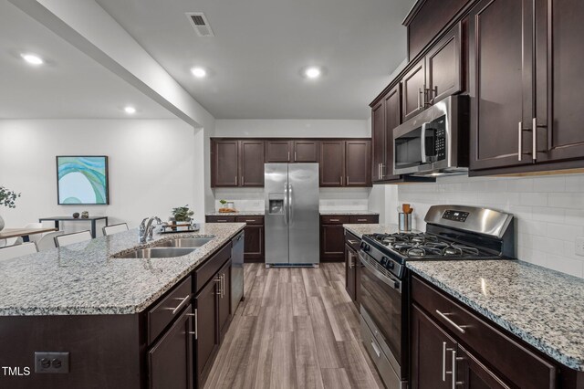 kitchen featuring stainless steel appliances, a sink, dark brown cabinets, decorative backsplash, and light wood-type flooring