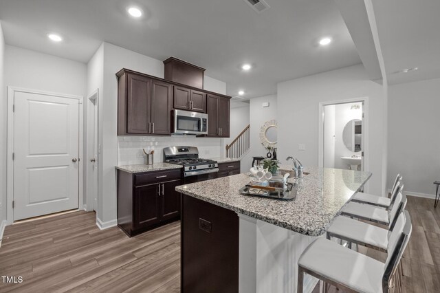 kitchen with stainless steel appliances, light wood-style flooring, light stone counters, a breakfast bar, and a center island with sink