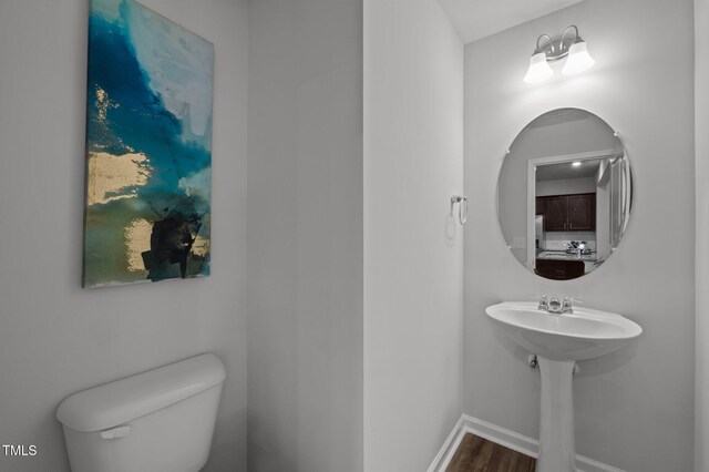 half bath featuring wood finished floors, toilet, and baseboards