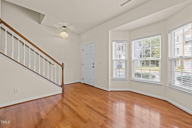 foyer featuring visible vents, baseboards, a notable chandelier, light wood-style floors, and stairs