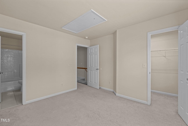 unfurnished bedroom featuring a walk in closet, attic access, carpet floors, baseboards, and a closet