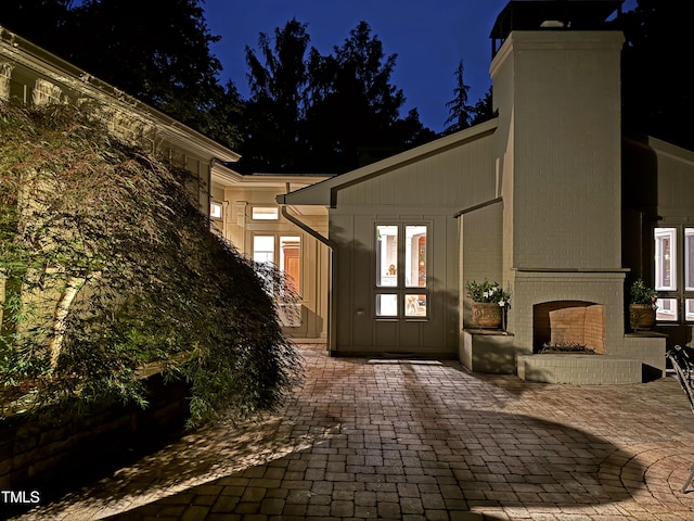 3915 Nottaway Rd, Durham, NC 27707 - exterior entry at twilight featuring an outdoor brick fireplace, a chimney, and a patio