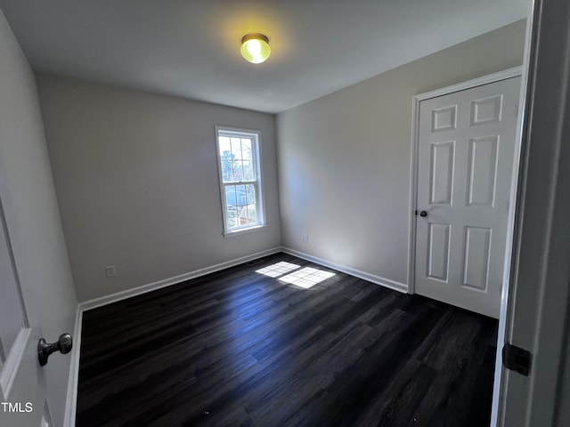 unfurnished room with dark wood-type flooring and baseboards