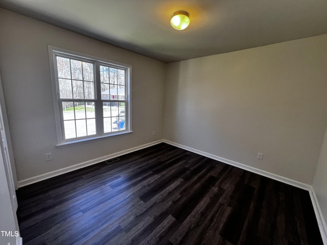 unfurnished room featuring dark wood finished floors, visible vents, and baseboards