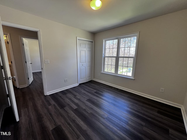 unfurnished bedroom with visible vents, dark wood-style floors, baseboards, and a closet