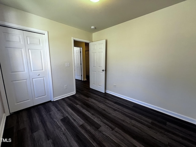 unfurnished bedroom with dark wood-style floors, a closet, and baseboards