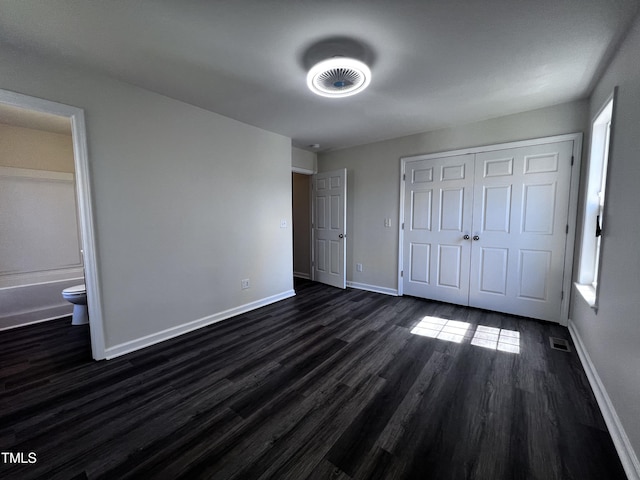 unfurnished bedroom featuring visible vents, baseboards, dark wood-style flooring, a closet, and connected bathroom